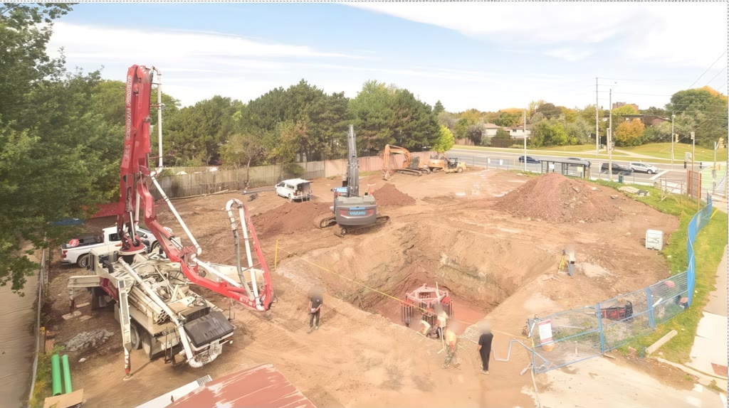 A concrete pump truck with its boom over the deep excavation for the crane footing, with excavators and soil piles across the site and the street beyond.